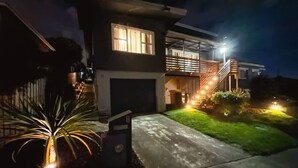 Una casa moderna de dos pisos con garaje, ventanas iluminadas y un patio delantero bien iluminado.