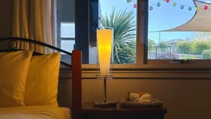 Una cama con un almohadón, una mesita de noche con una lámpara y vistas al exterior a través de una ventana.