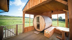 A wooden sauna with a large barrel, wooden benches, and a view of a green field. - Atlas (Nairn)