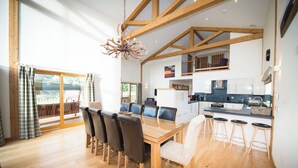 A spacious dining area with a wooden table and chairs, a chandelier, and a view of the outdoors through large windows. - Atlas (Nairn)