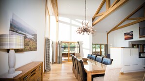 A spacious dining area with a wooden table and chairs, a chandelier, and a view of the outdoors. - Atlas (Nairn)
