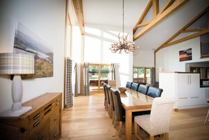 Un comedor amplio con una mesa y sillas de madera, una araña y vistas al exterior.