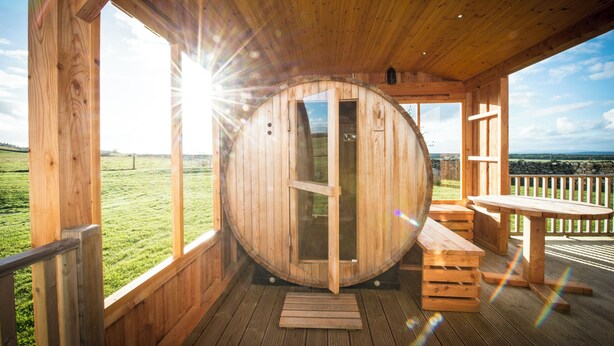Una cabaña de madera con un ventanal circular grande, terraza de madera y una mesa.