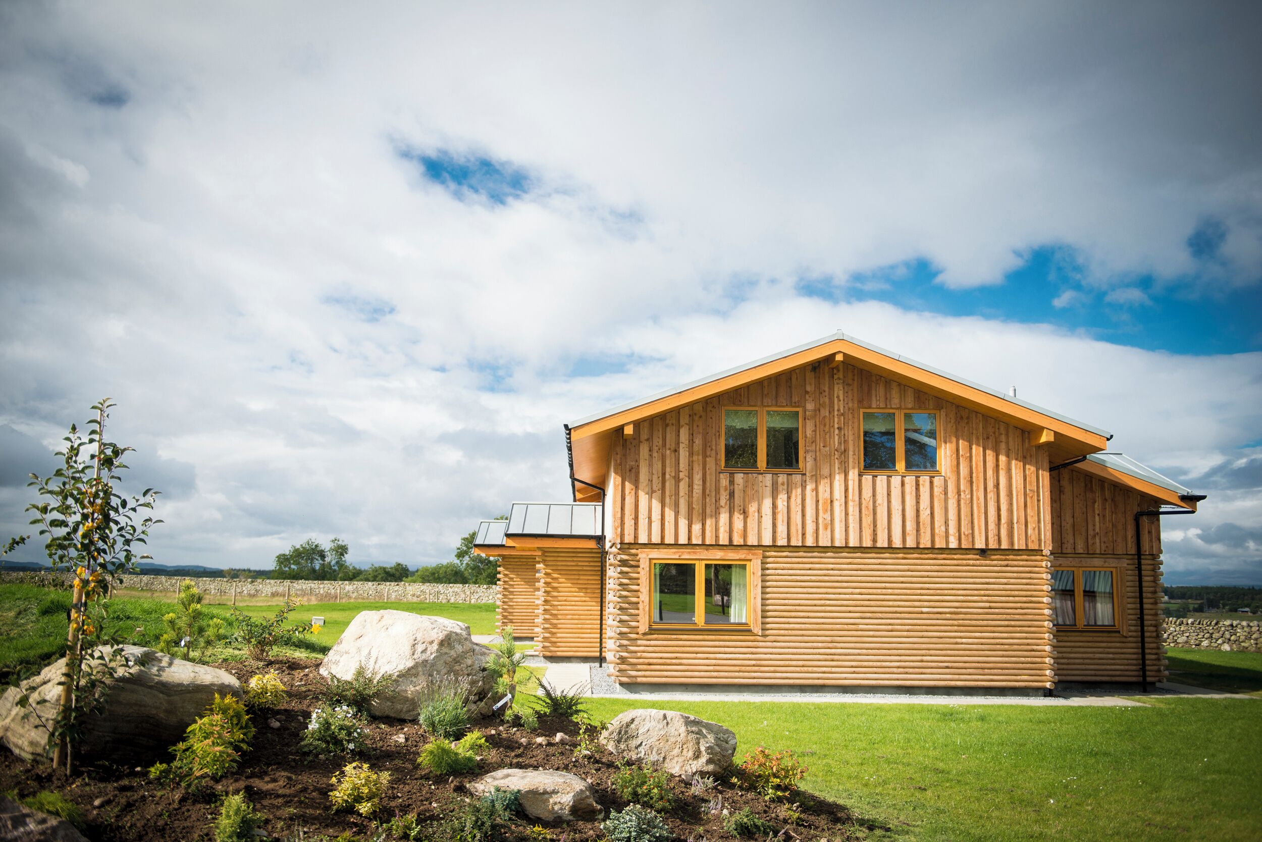 A wooden log cabin with a sloped roof, large windows, and a well-maintained lawn.