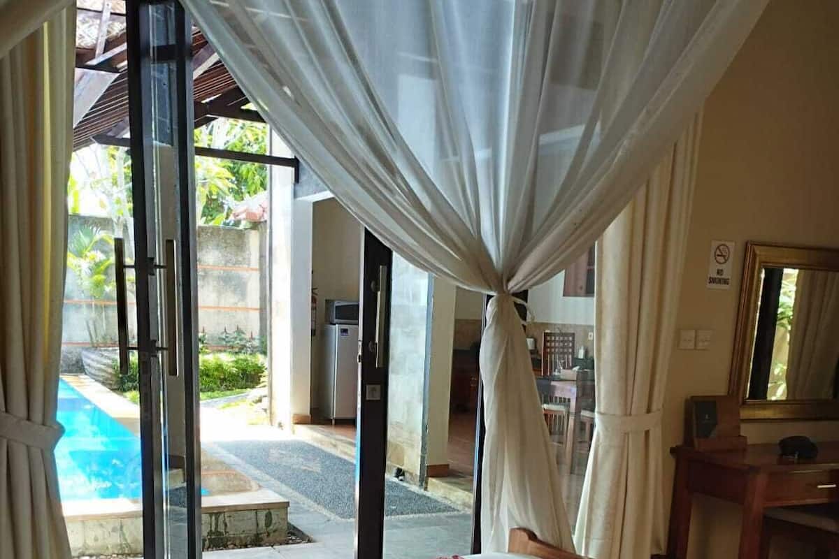 A bedroom with a bed, a desk, a chair, and a view of an outdoor swimming pool.