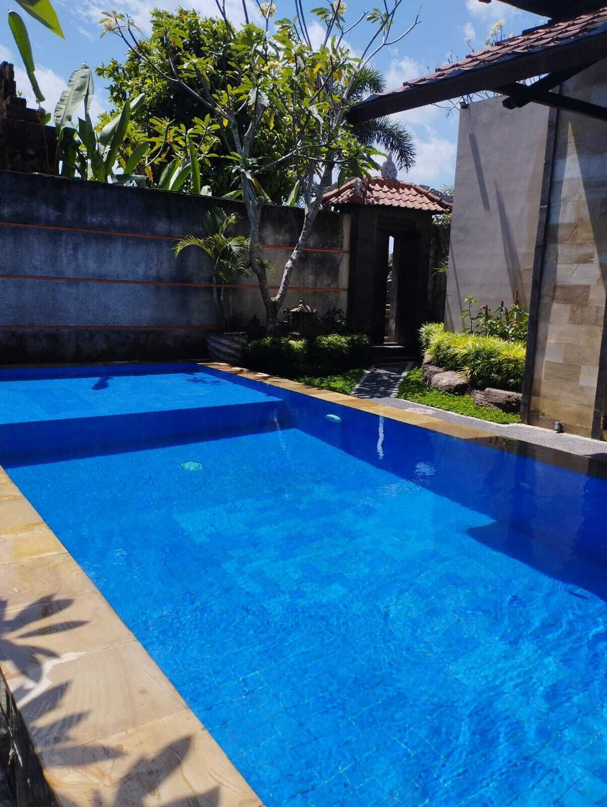 A rectangular swimming pool with clear blue water, surrounded by a concrete wall and a stone building with a tiled roof.