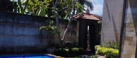 Una piscina rectangular con agua azul cristalina, rodeada por un muro de hormigón y un edificio de piedra con techo de tejas.