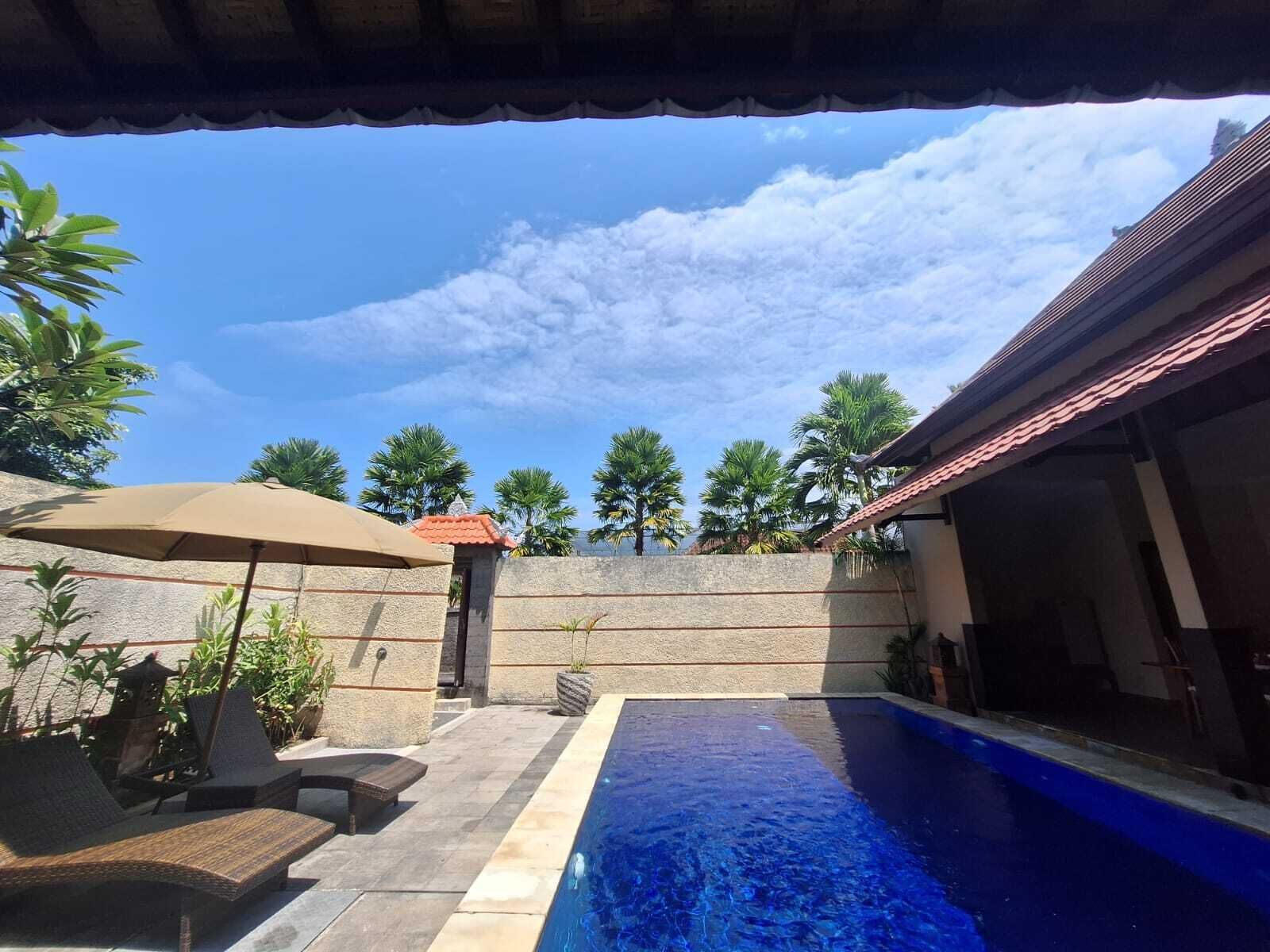 A swimming pool with a stone wall, lounge chairs, and an umbrella.