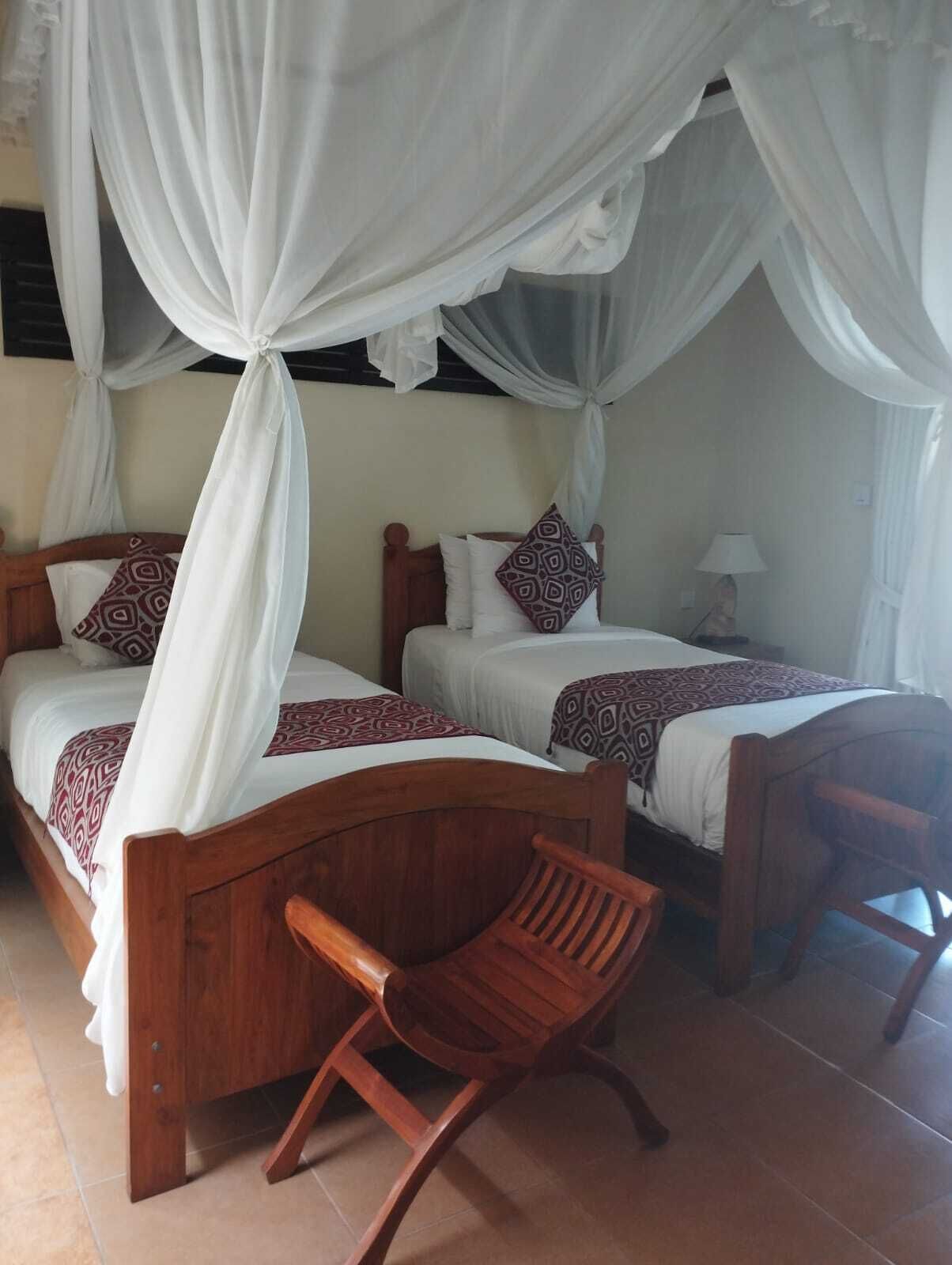 A room with two beds, each with a wooden headboard and white bedding. There is a wooden chair in the center of the room.