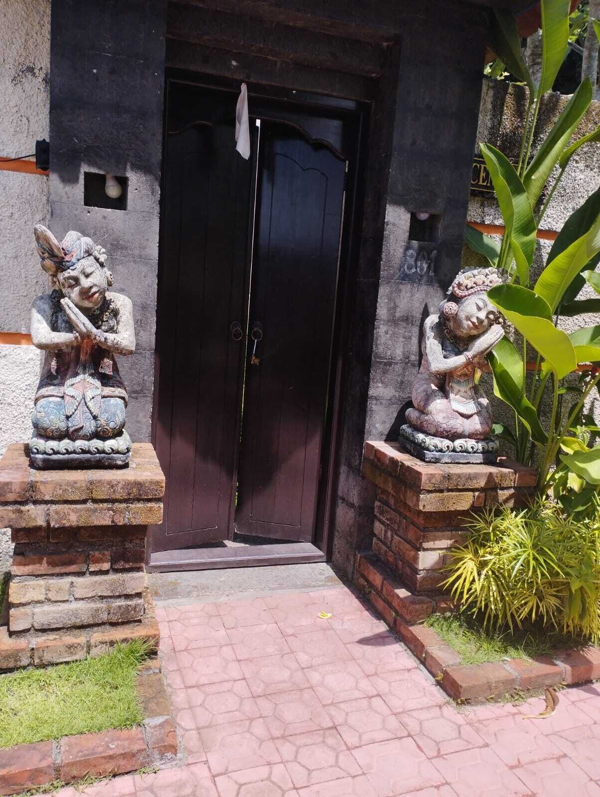 A building entrance with a dark wooden door, flanked by two stone statues on pedestals.