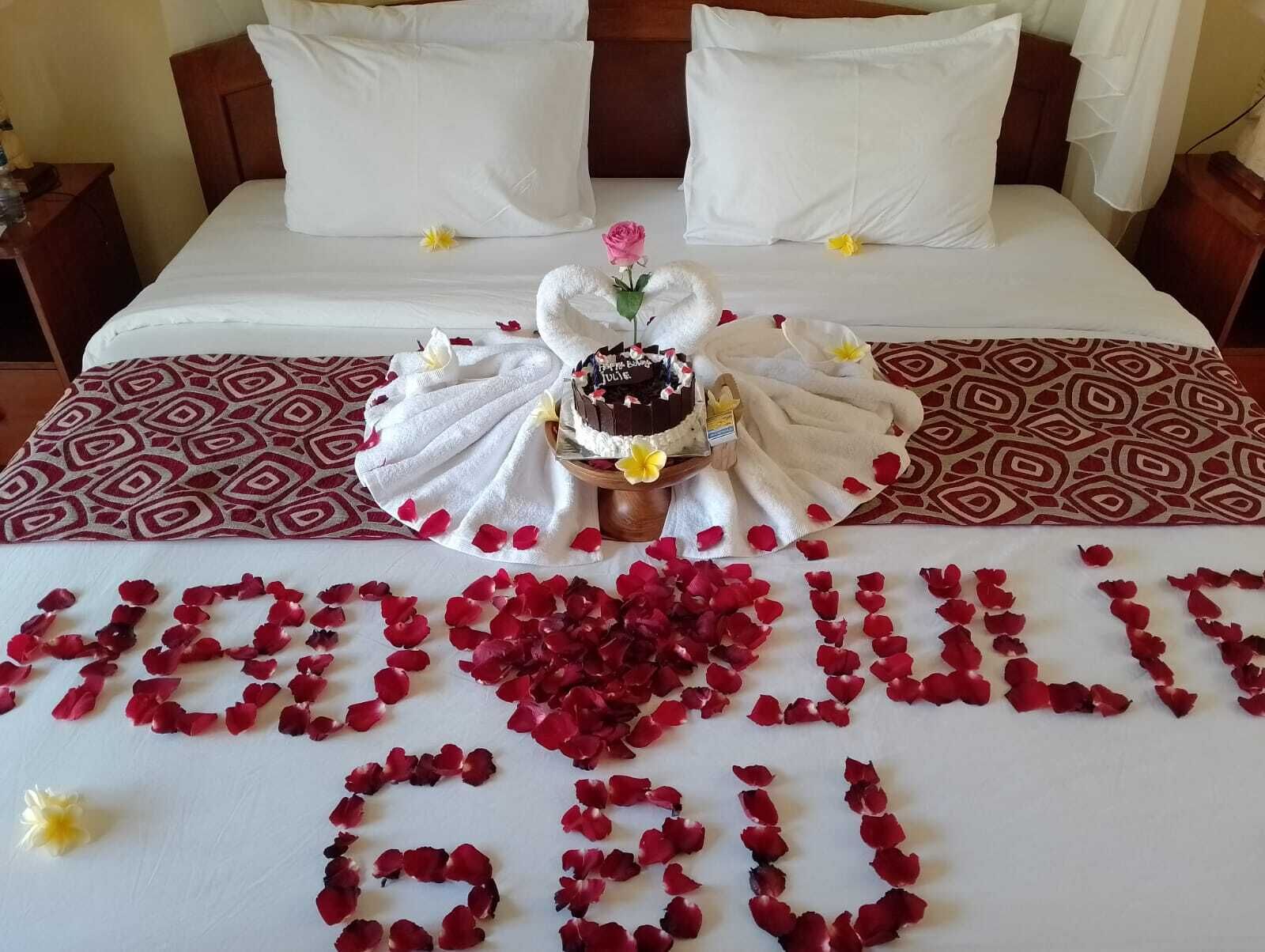 Un lit décoré d’un bouquet de fleurs, d’un gâteau et de pétales de rose disposés sur le couvre-lit.