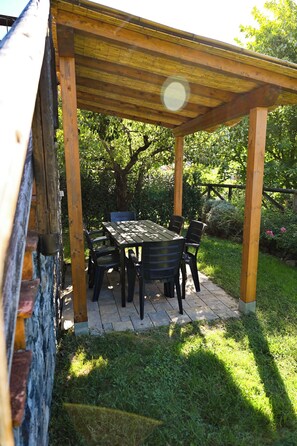 A covered outdoor seating area with a table and chairs, surrounded by greenery. - Ca' Livio (Crespiano)