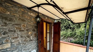 A covered patio with stone walls, a wooden door, and a white table and chair. - Apartment Ca' Livio (Crespiano)