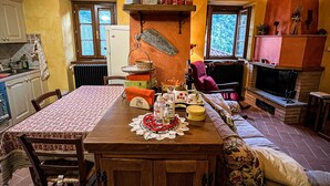 A cozy kitchen with wooden cabinets, a dining table with a patterned tablecloth, and a fireplace. - Apartment Ca' Livio (Crespiano)