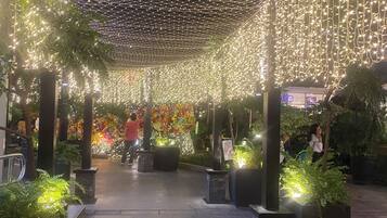 An indoor atrium with a netted ceiling and string lights, surrounded by potted plants and a floral wall.