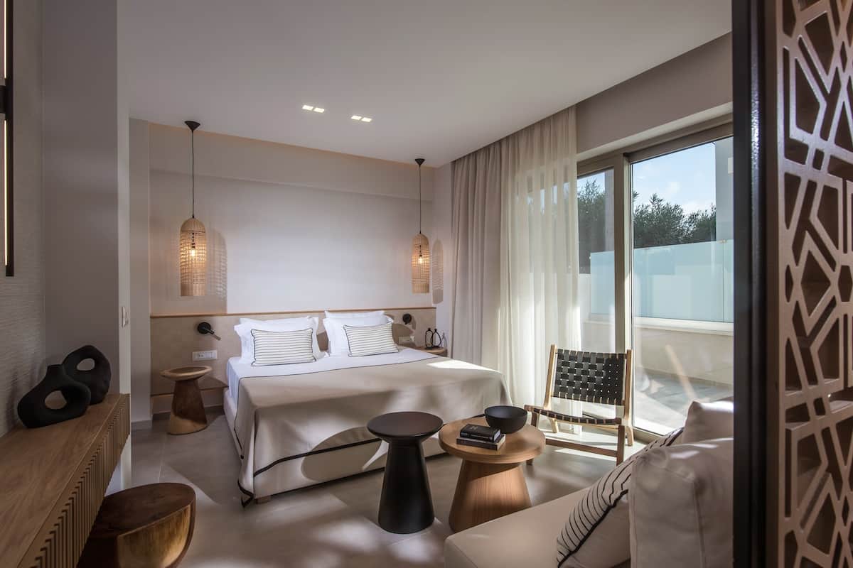 Ein modernes Hotelzimmer mit einem großen Bett, zwei Nachttischen, einem Sofa und einem Balkon mit Blick.