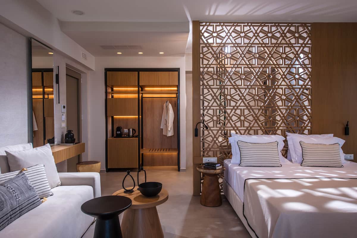 Ein modernes Hotelzimmer mit Bett, einer Couch, einem kleinen Tisch, einer Holzwand und einem Badezimmer mit Handtuchhalter.