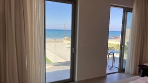 A hotel room with a large sliding glass door leading to a balcony with a view of the beach and ocean. - Niriides Palace (Hersonissos)