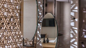 A modern bathroom with a large oval mirror, a white sink, and a wooden decorative panel in the background. - Niriides Palace (Hersonissos)