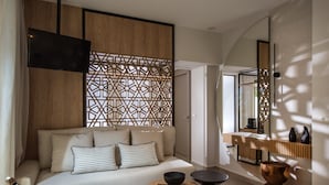 A modern hotel room with a large bed, a wooden partition, a TV, a small table, and a chair. - Niriides Palace (Hersonissos)