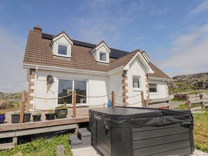 A two-story house with a tiled roof, a deck with potted plants, and a hot tub.