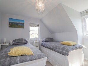 A bedroom with two beds, a window, a painting, and a chandelier.