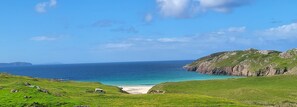 A coastal landscape with a grassy area, a small building, and a view of the sea and distant landforms.