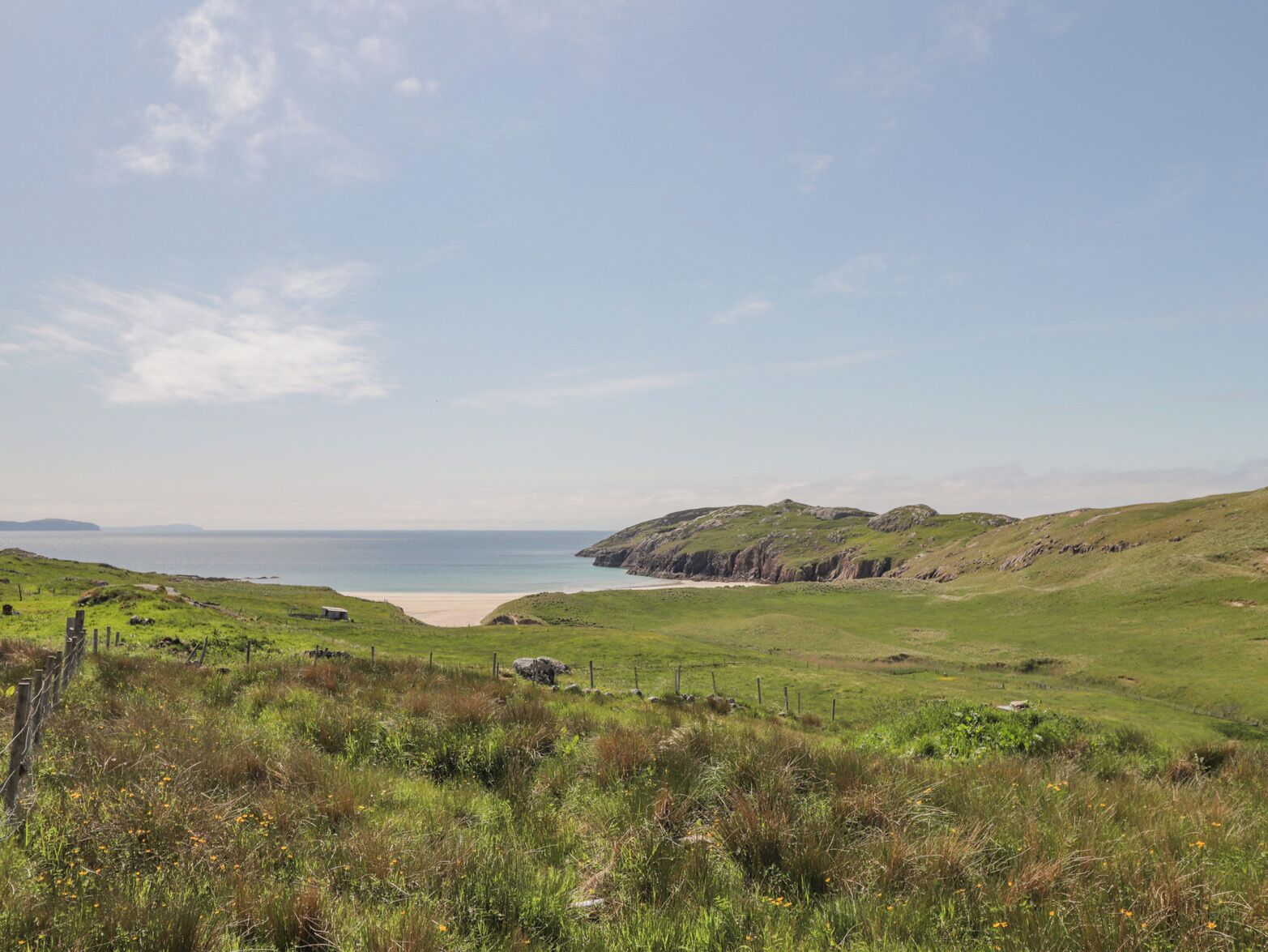 Eine Küstenlandschaft mit grünen Hügeln, einem Sandstrand und blauem Himmel.