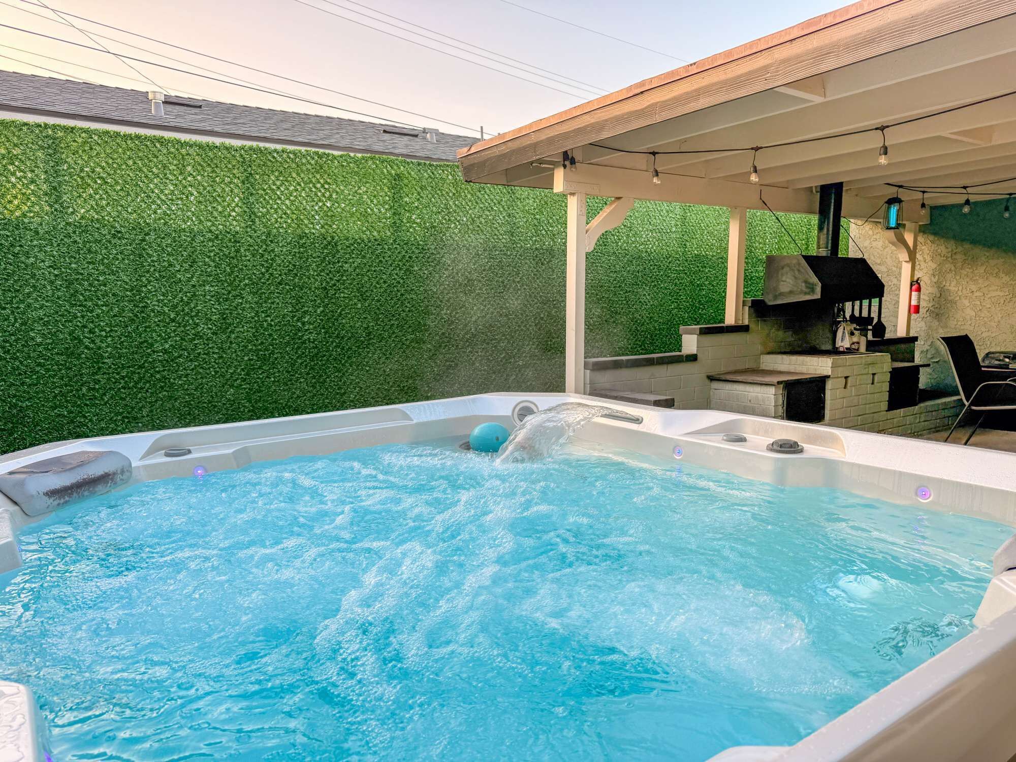 A hot tub with water flowing, surrounded by a green wall and a wooden pergola.