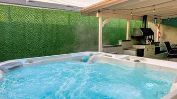 A hot tub with water flowing, surrounded by a green wall and a wooden pergola.