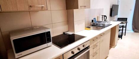 A modern kitchen with wooden cabinets, a built-in microwave, a stove, and a dining area with a chair and table.