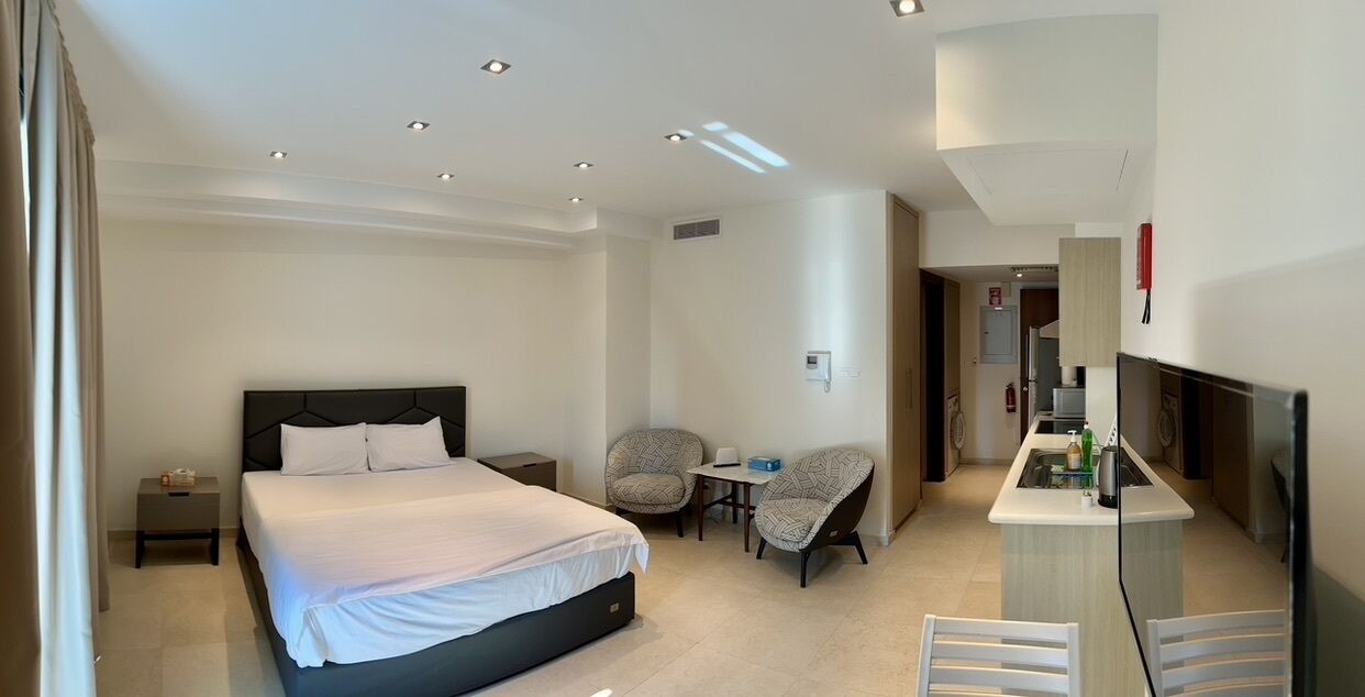 A hotel room with a bed, two chairs, a small table, a TV, and a kitchenette.