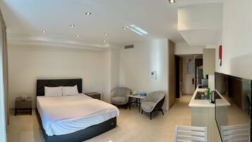A hotel room with a bed, two chairs, a small table, a TV, and a kitchenette.