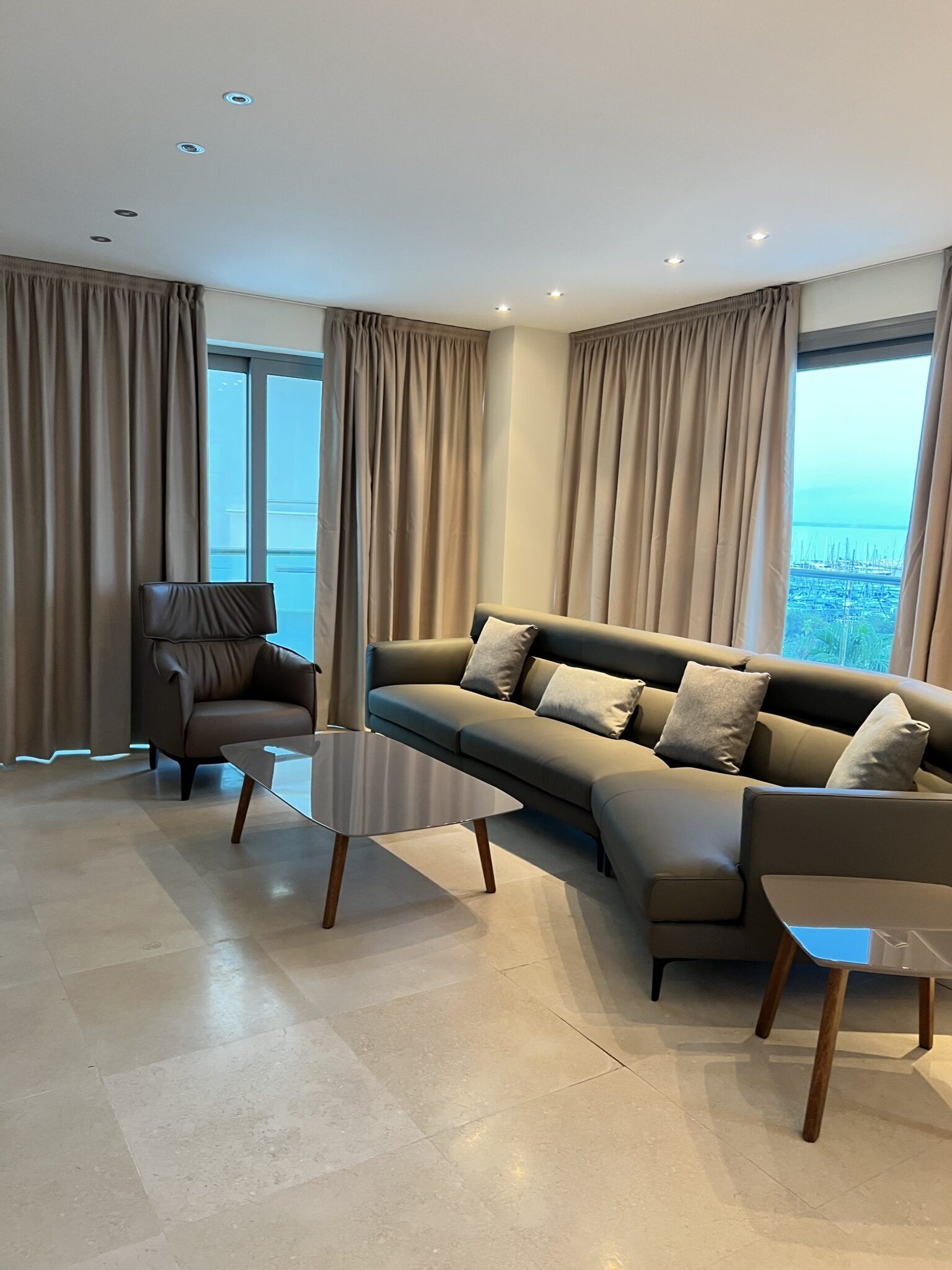 A modern living room with a sectional sofa, two side tables, and a view of the sea through large windows.