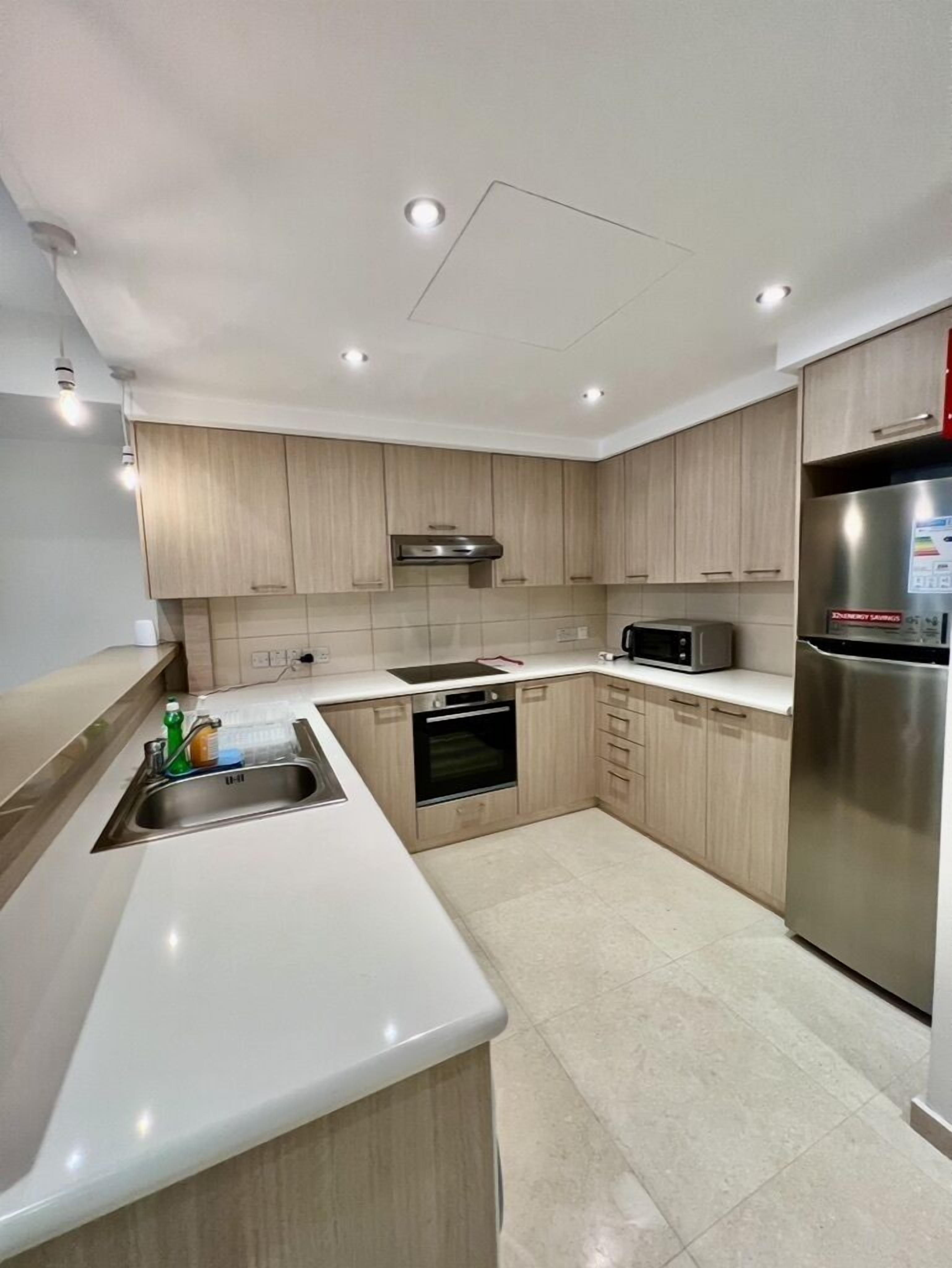 A modern kitchen with light wood cabinets, stainless steel appliances, and a white countertop.