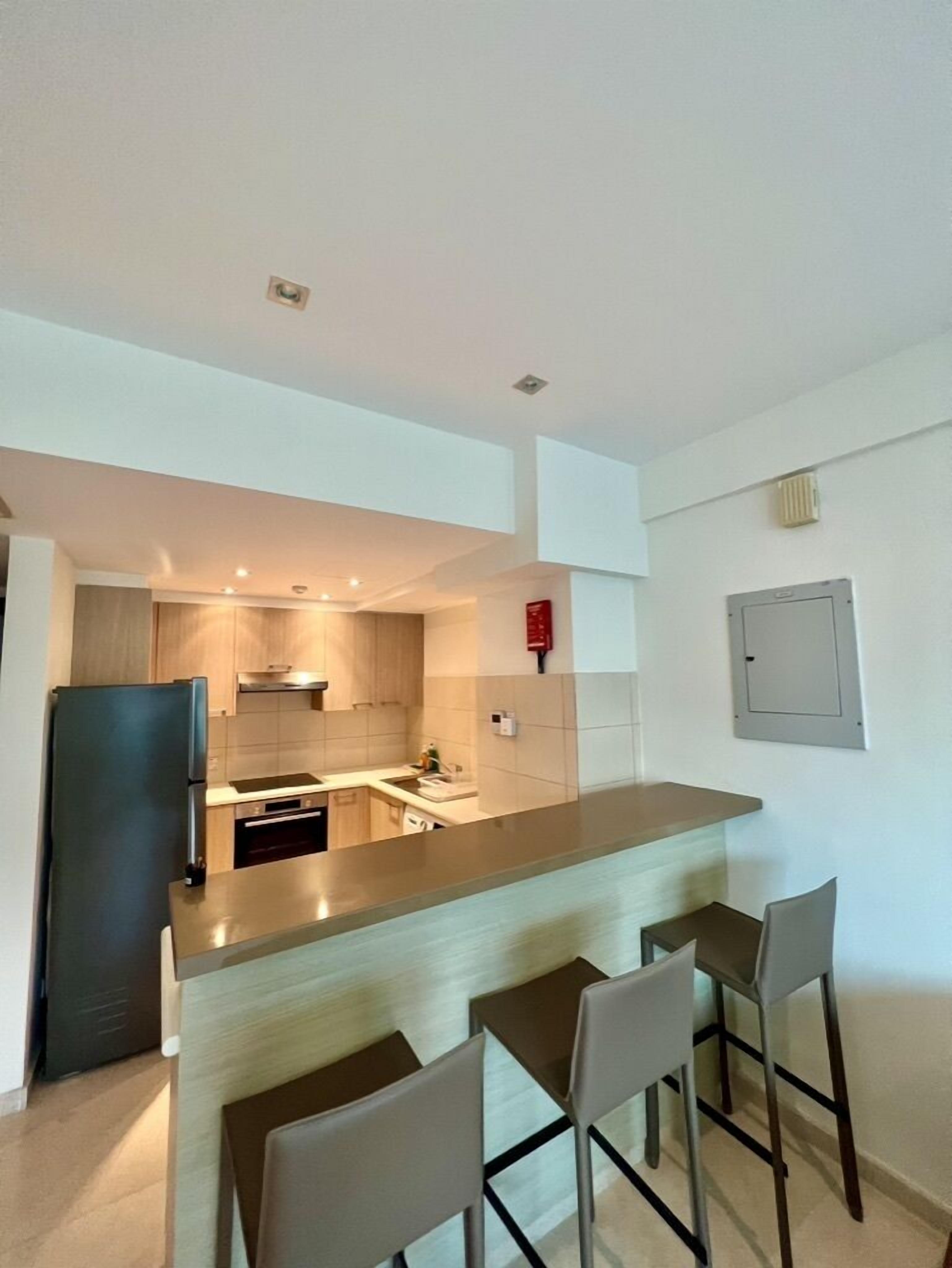 A modern kitchen with a central island, bar stools, and a built-in refrigerator.