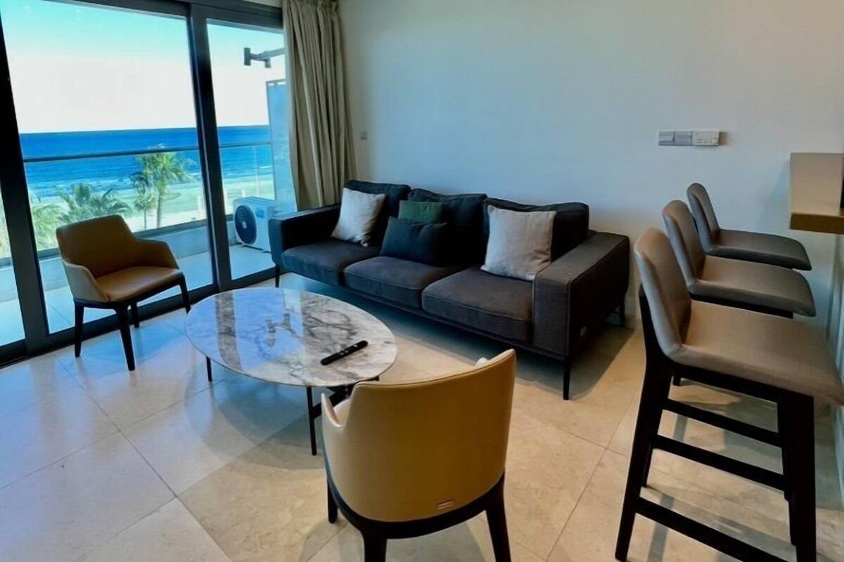 A modern living room with a sofa, chairs, a coffee table, and a view of the ocean.