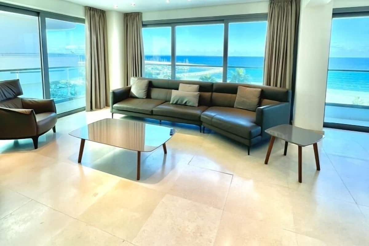 A modern living room with a large sofa, two coffee tables, and a view of the ocean.