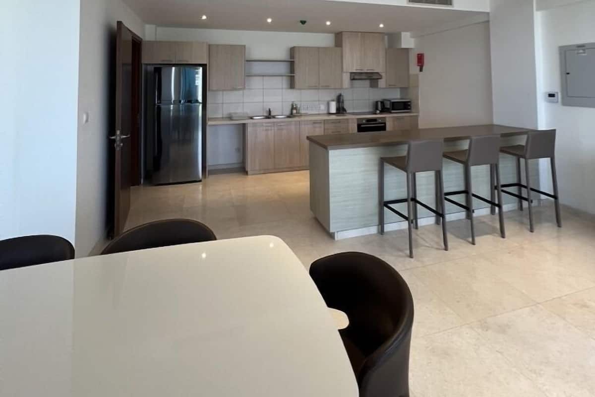 A modern kitchen with a central island, recessed lighting, and a dining area with chairs.