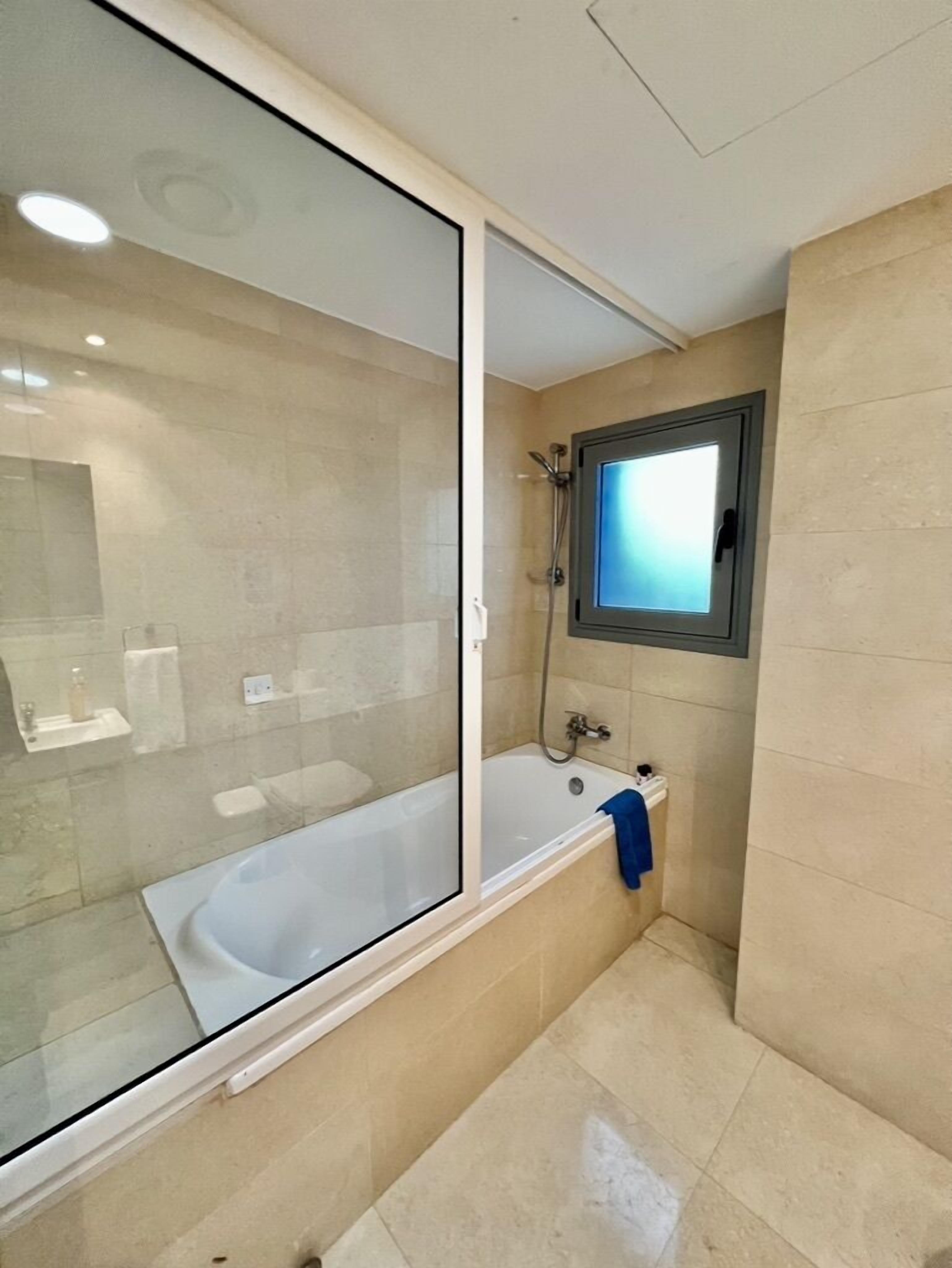 A modern bathroom with a glass-enclosed shower, a built-in bathtub, and a small window.