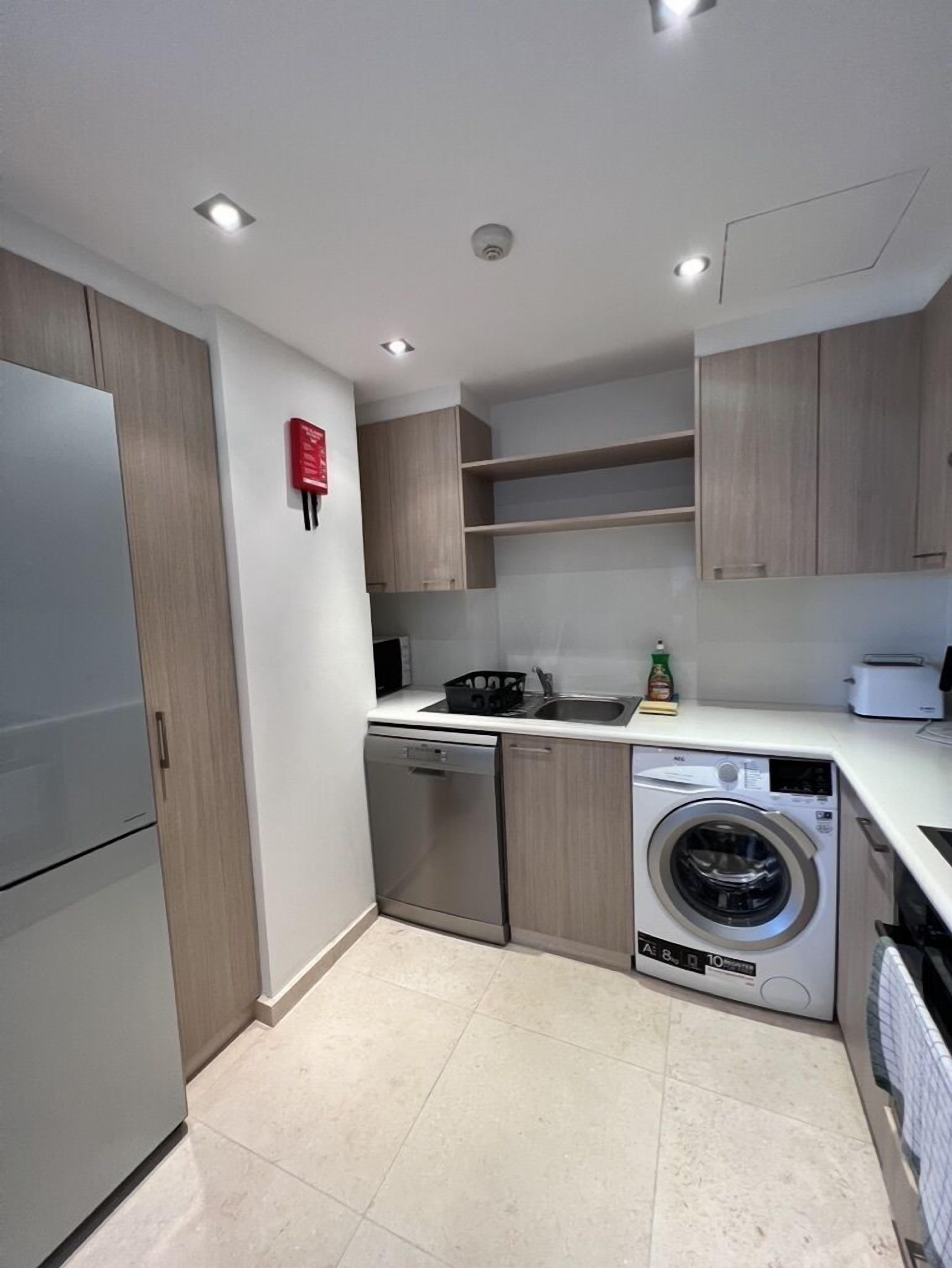 A compact kitchen with a built-in dishwasher, a washing machine, and a microwave.