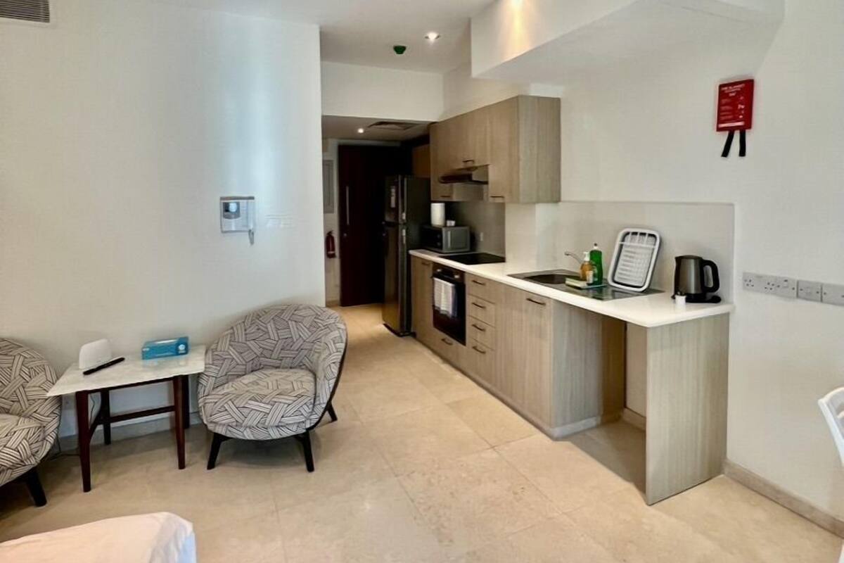 A modern kitchen with a built-in oven, microwave, and sink. There is a dining area with two patterned chairs and a small table.