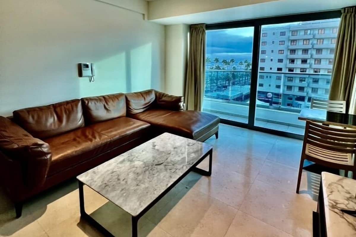 A modern living room with a brown leather sofa, a marble coffee table, and a view of a cityscape through large windows.
