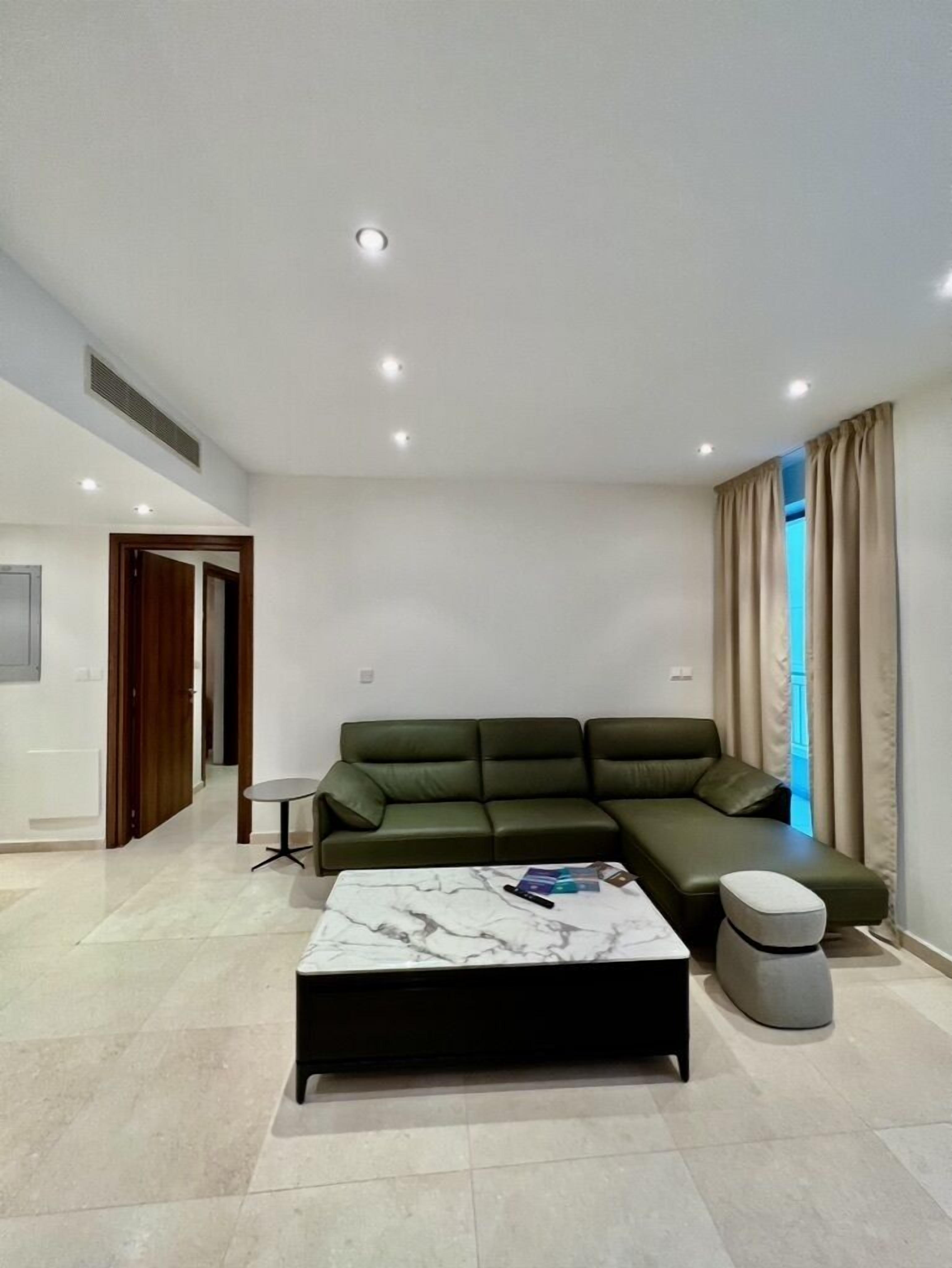 Un salon moderne avec un canapé d’angle, une table basse en marbre et une petite table d’appoint.