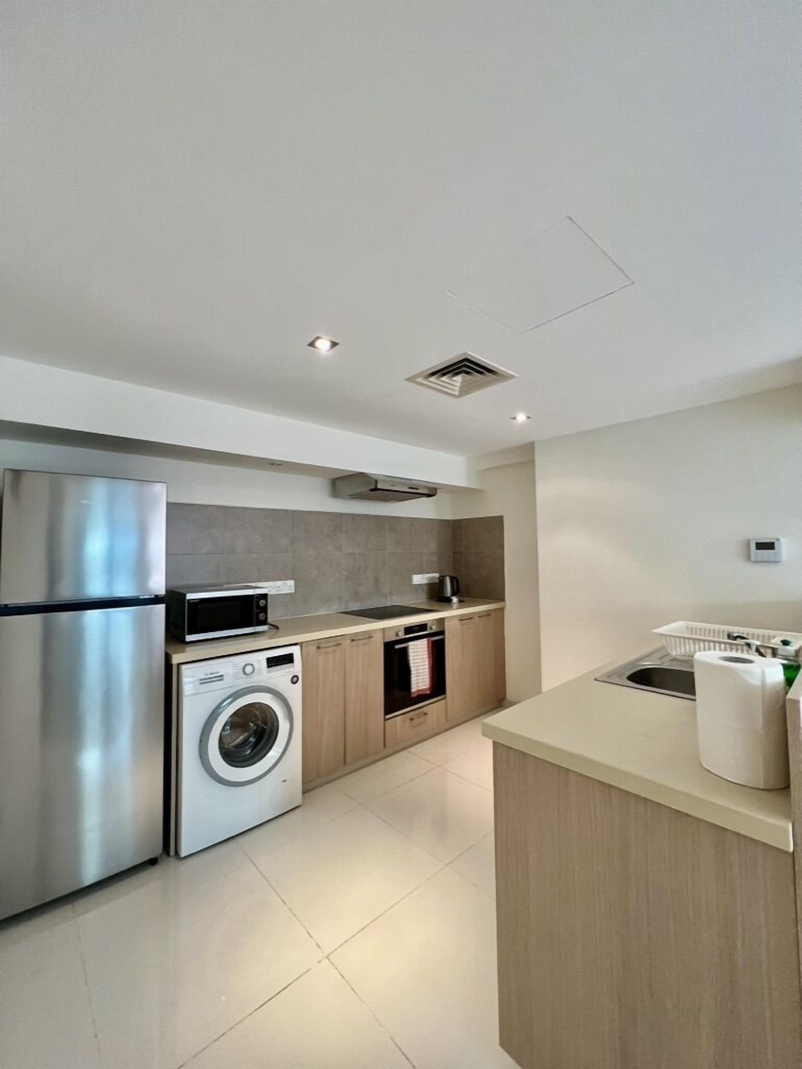 Una cocina moderna con un refrigerador de acero inoxidable, lavadora integrada, microondas y horno pequeño.