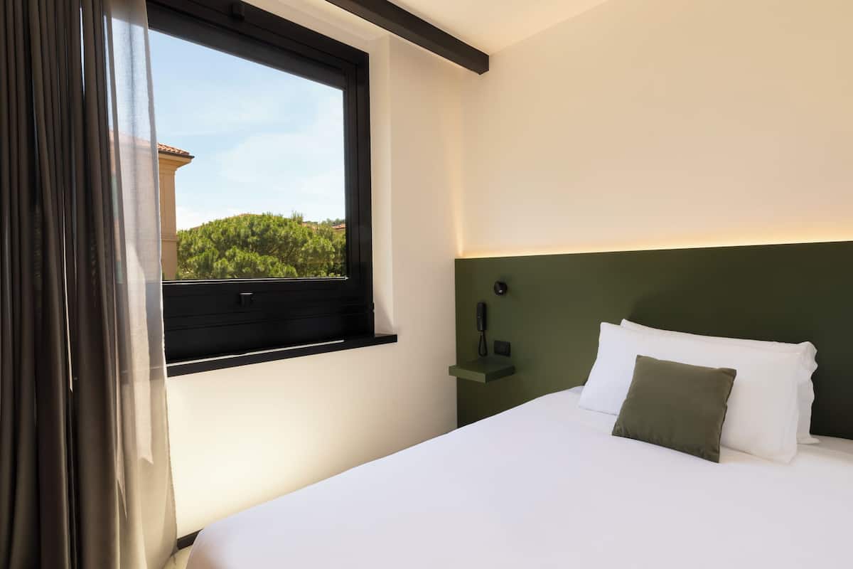 A hotel room with a bed, a nightstand, a phone, and a window with curtains.