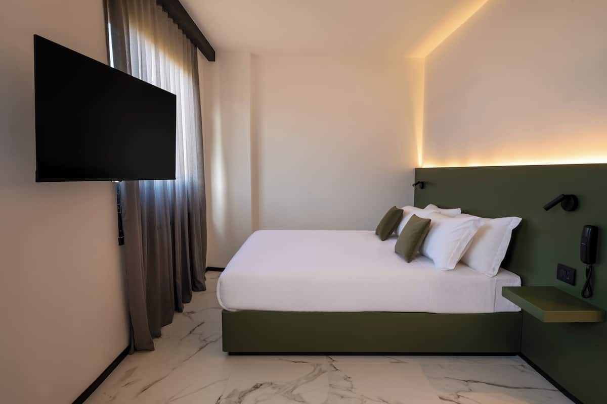 A modern hotel room with a large bed, a flat-screen TV mounted on the wall, a bedside table with a phone, and a marble floor.