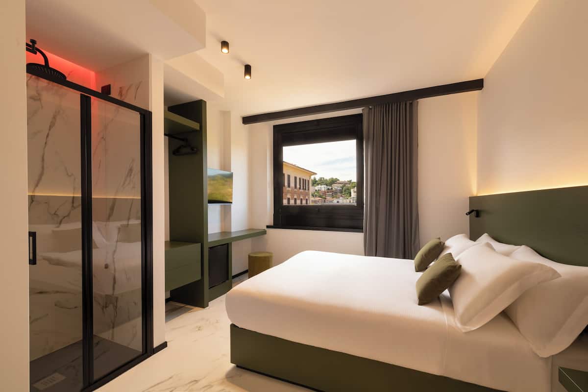 A modern bedroom with a large bed, a walk-in closet, and a window with a view of buildings.