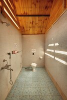 Un baño pequeño y cerrado con techo de madera, inodoro, ducha y suelo de baldosas.
