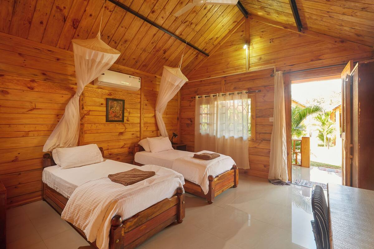 A wooden cabin with two beds, a ceiling fan, and a view of the outdoors.